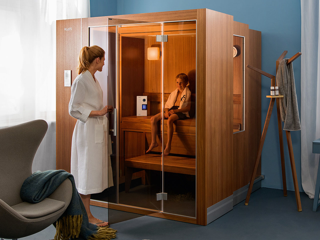 Frau öffnet luxuriöse Sauna mit Kind darin, im gemütlichen, modern eingerichteten Raum.