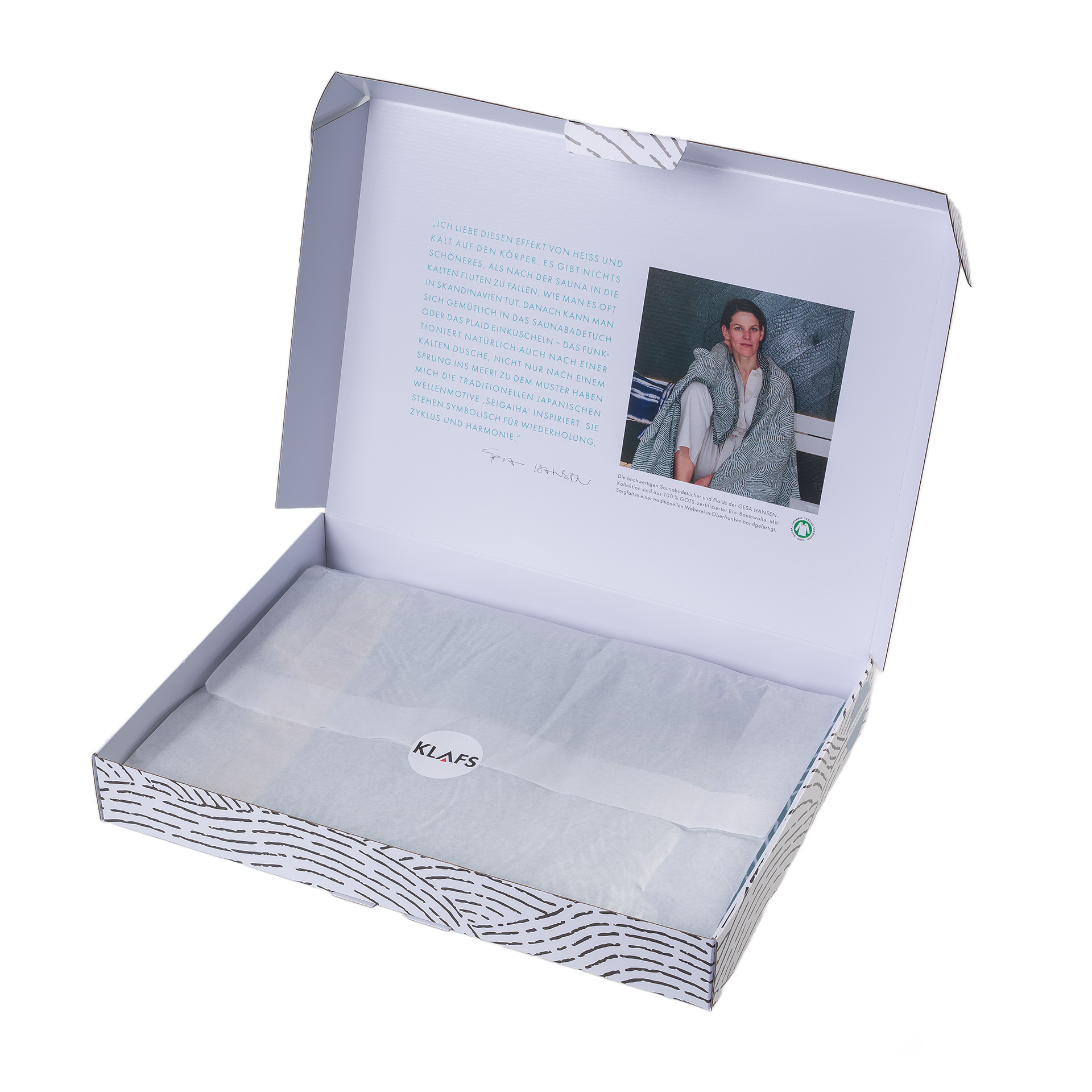 Geschenkbox geöffnet, mit Text und Bild innen, Papier mit "KLAFS" Aufschrift bedeckt luxuriösen Inhalt.